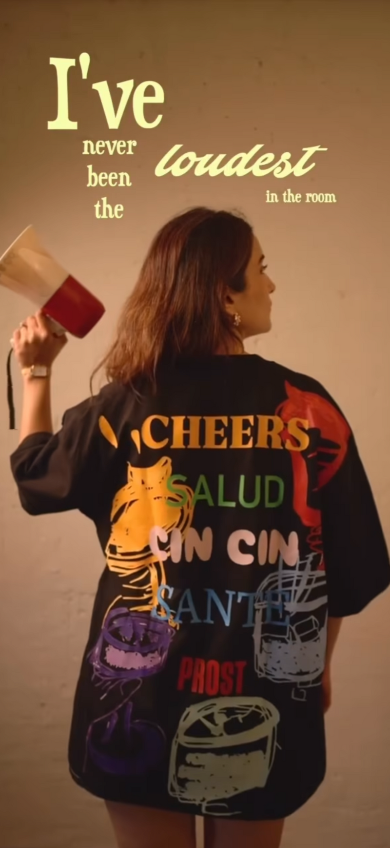 Person wearing a colorful oversized t-shirt with text and graphics, holding a microphone.